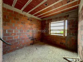 Vista interna de uma sala com paredes de tijolo aparente e piso de terra.
