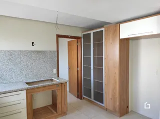 Vista interna de uma cozinha com armários de madeira e bancada clara.