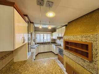 Vista interna de uma cozinha com armários brancos e detalhes em pedra.