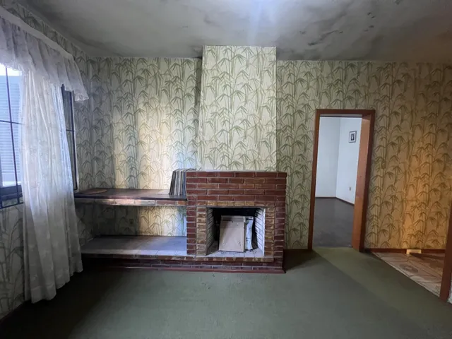 Sala de estar com lareira de tijolos e papel de parede de folhagem.