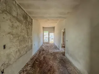 Corredor interno de uma residência com paredes brancas e piso rústico.