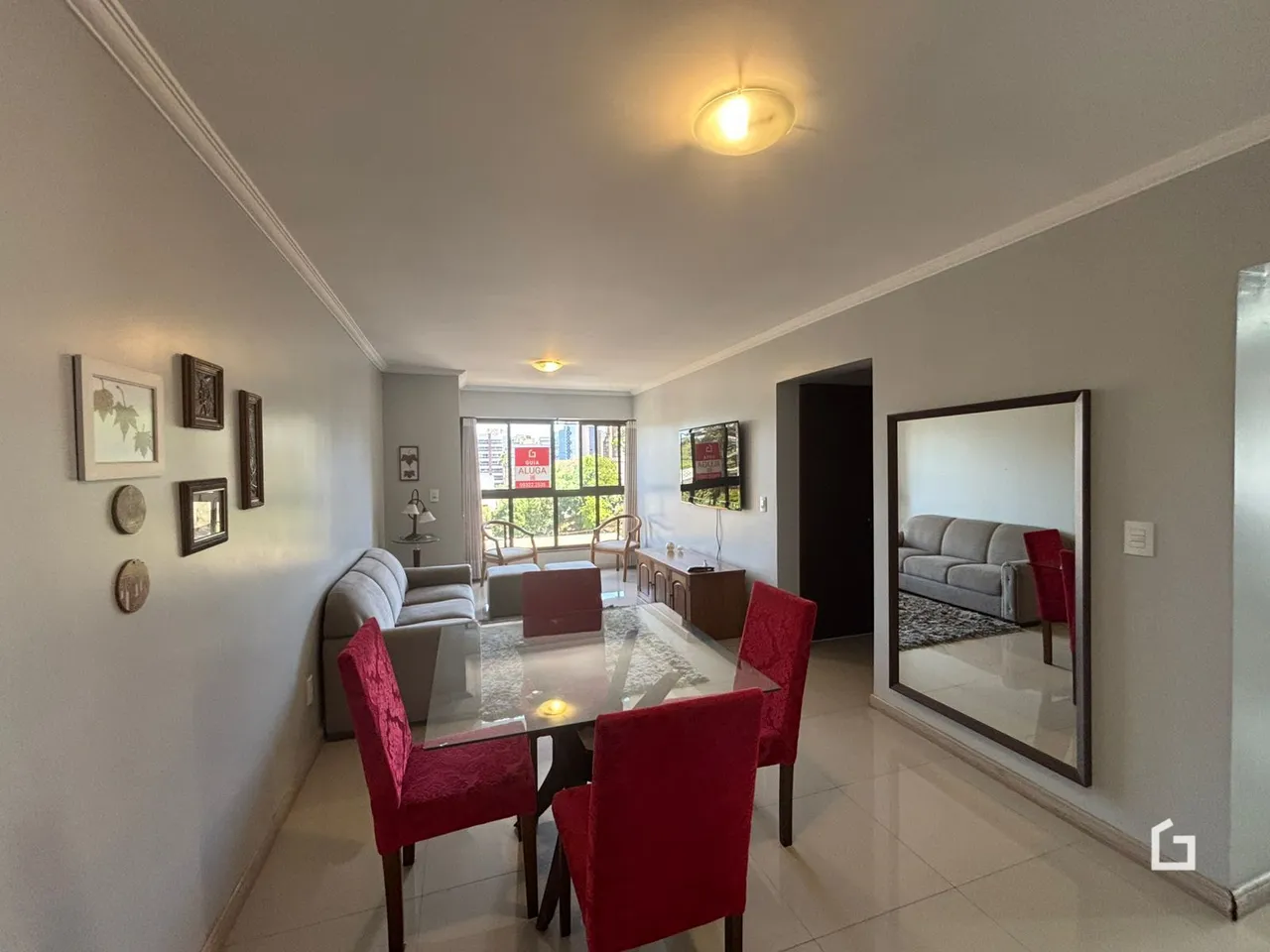 Sala de jantar com mesa de vidro e cadeiras vermelhas.