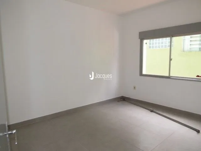 Interior de uma sala de estar vazia com paredes brancas e piso claro.
