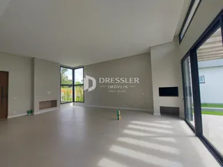 Ambiente interno de uma sala ampla com piso claro e grandes janelas.