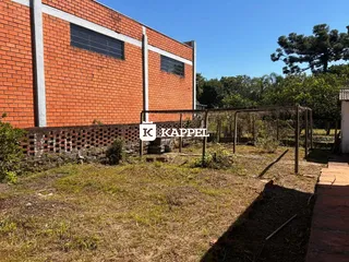 Fachada de um imóvel com alvenaria de tijolos e um terreno com vegetação rasteira.