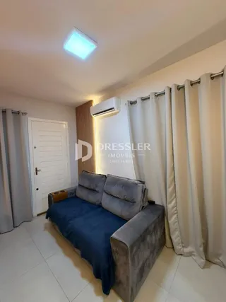 A sala de estar mostra um sofá e cortinas brancas em um imóvel.