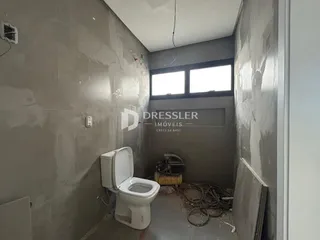 Interior de um corredor com paredes em fase de acabamento e um vaso sanitário.