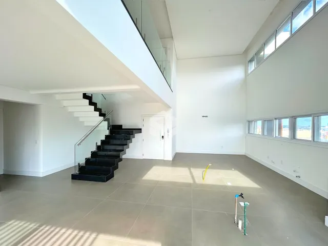 Ambiente interno de uma sala de estar com escadaria e grandes janelas.