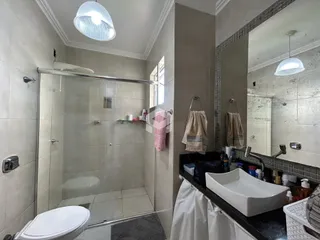 Foto interna de um banheiro com box de vidro e azulejos brancos.