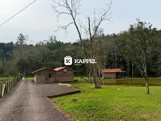 Vista externa de uma propriedade rural com cabanas próximas a um lago.