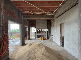 Interior de uma estrutura em construção com paredes de tijolo aparente e piso de terra.
