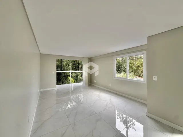 Ambiente interno amplo com piso de porcelanato claro e vista para a mata.