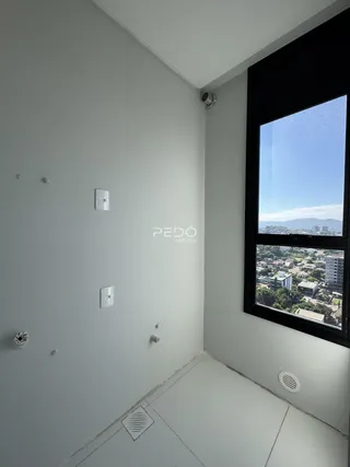 Vista de um canto de cômodo interno com parede branca e janela de vista para a cidade.