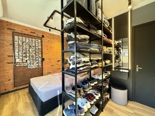 Quarto com parede de tijolos e estante de metal preenchida com roupas.