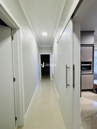 Corredor interno de uma residência com paredes brancas e piso claro.