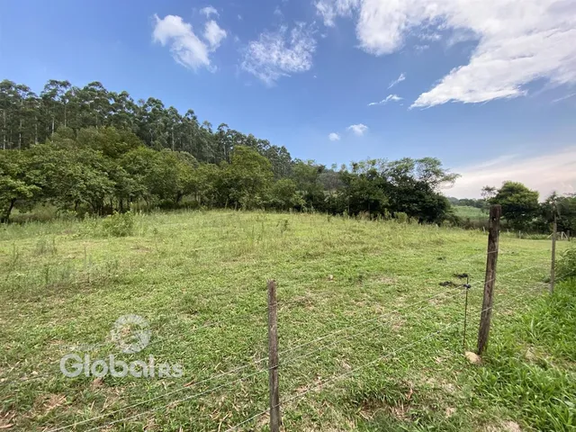 Campo gramado com cerca de arame em uma paisagem rural.