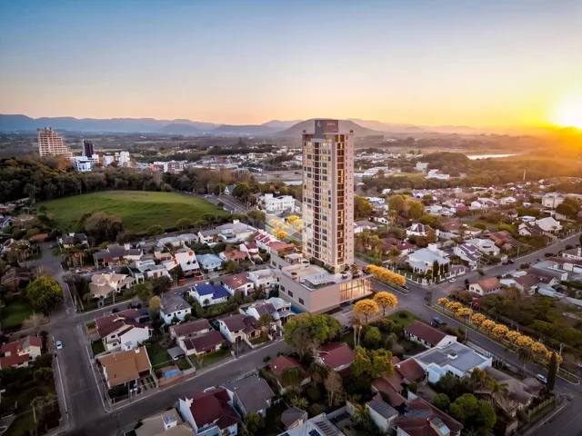 Vista aérea de um bairro residencial com um edifício alto no centro e paisagem de montanhas ao fundo.