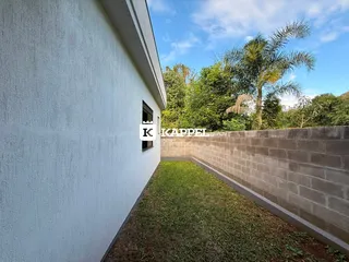 A foto mostra a fachada branca de um imóvel com um jardim estreito e uma cerca de concreto.