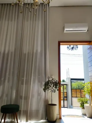 Cortinas brancas e um lustre são visíveis no interior da sala de estar.