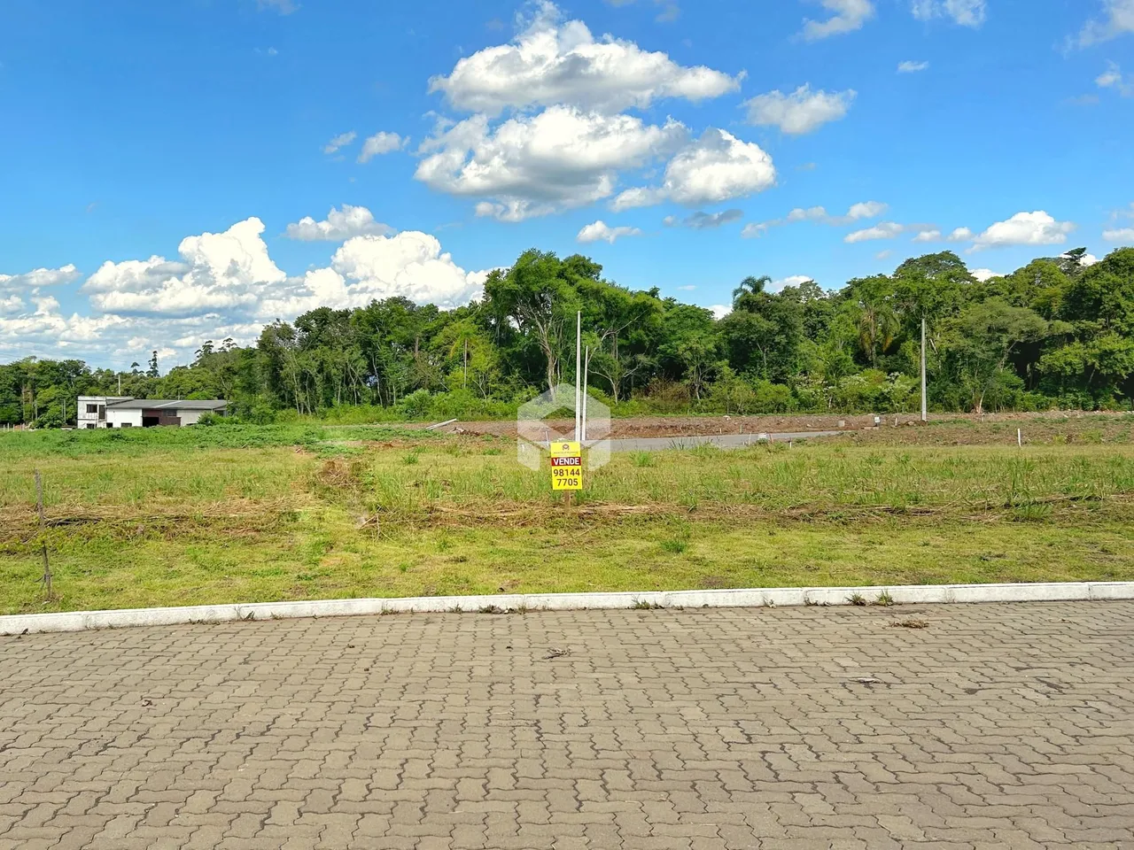 Vista externa de um terreno com gramado e vegetação ao fundo.