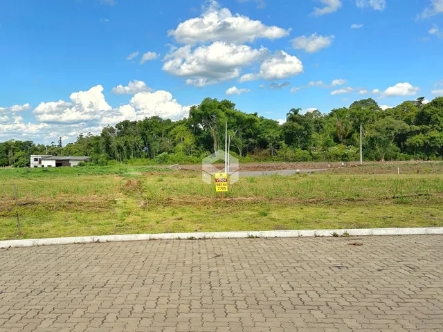 Vista externa de um terreno com gramado e vegetação ao fundo.