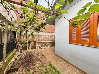 Vista da fachada de uma residência com vegetação e calçada de tijolos.