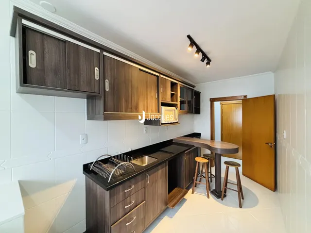 Vista interna de uma cozinha com armários de madeira escura e piso de cerâmica.