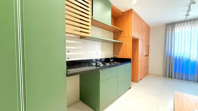 Uma cozinha moderna com armários verdes e bancada escura.