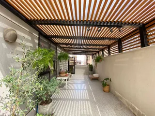 Corredor externo com vegetação e estrutura de madeira no imóvel.