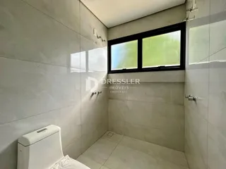 Banheiro com revestimento cerâmico branco e janela com vista para o exterior.