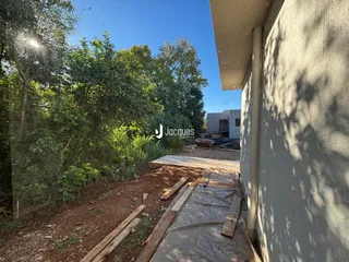 Vista externa de uma propriedade em construção com vegetação densa ao lado da parede.