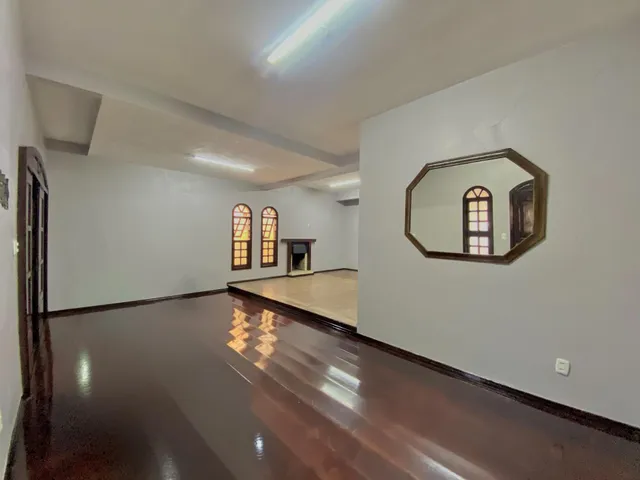 Uma sala ampla com piso de madeira escura e paredes brancas.