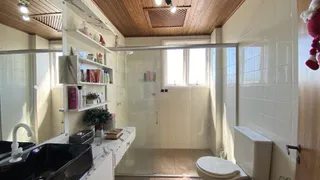 Banheiro com bancada de mármore e box de vidro transparente.