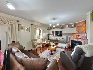 Sala de estar com sofás de couro marrom e piso de madeira em uma residência.