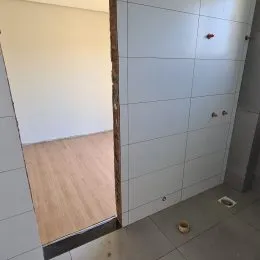 Vista parcial de um ambiente interno com piso de madeira clara e paredes brancas.