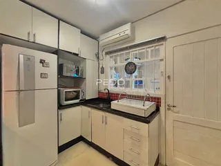 Vista interna de uma cozinha com armários brancos e bancadas escuras.