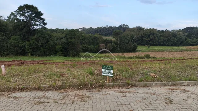Vista de um campo aberto com vegetação densa ao fundo e uma placa de venda.