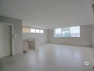 Ambiente interno de uma sala ampla com piso claro e janelas.