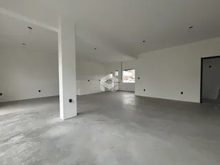 Interior de um espaço amplo com paredes brancas e piso de concreto.