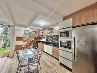 Interior de uma sala de estar com cozinha e escada em um apartamento no Brasil.