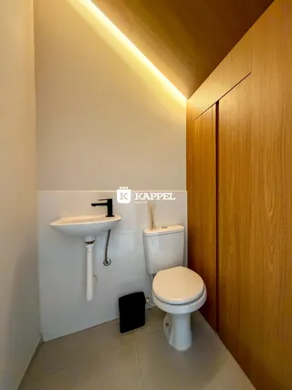 Foto de um banheiro com pia e vaso sanitário em um ambiente com revestimento branco e detalhes em madeira.