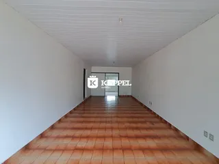 Corredor interno com piso de ladrilhos avermelhados e paredes brancas.