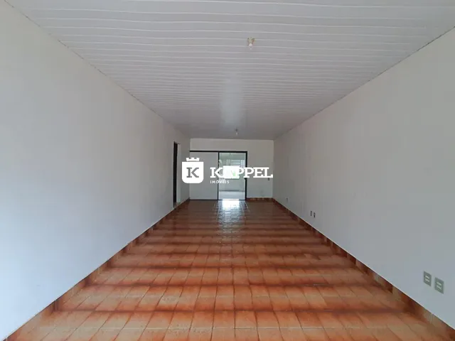 Corredor interno com piso de ladrilhos avermelhados e paredes brancas.