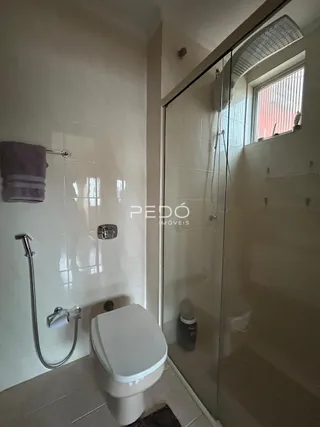 Foto interna de um banheiro com azulejos brancos e box de vidro.
