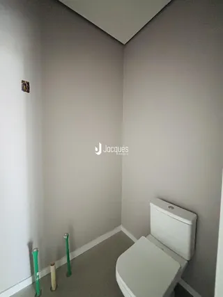 Canto de um ambiente interno com um vaso sanitário branco e paredes cinzas.