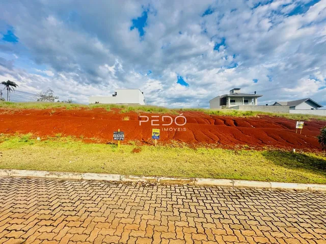 Vista externa de uma propriedade com terra avermelhada e casas ao fundo.