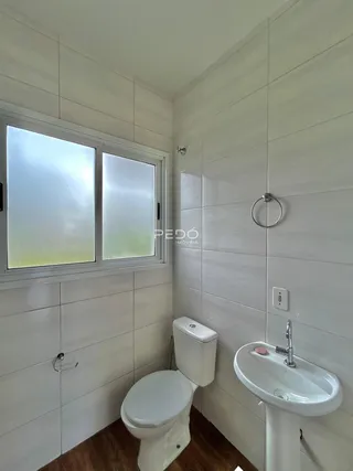 Banheiro com revestimento cerâmico branco e piso de madeira.