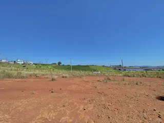 Vista panorâmica de um terreno com vegetação rasteira e colinas ao fundo sob um céu azul.