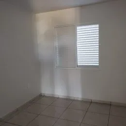 Foto de um cômodo interno com paredes brancas e janelas cobertas por persianas.