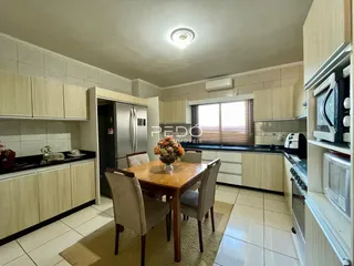 Vista de uma sala de jantar adjacente a uma cozinha com armários brancos.